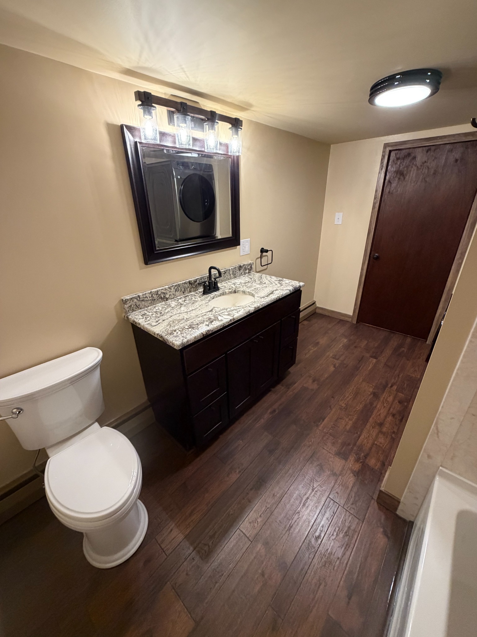 Warm traditional bathroom with dark vanity, granite countertop and wood-look flooring