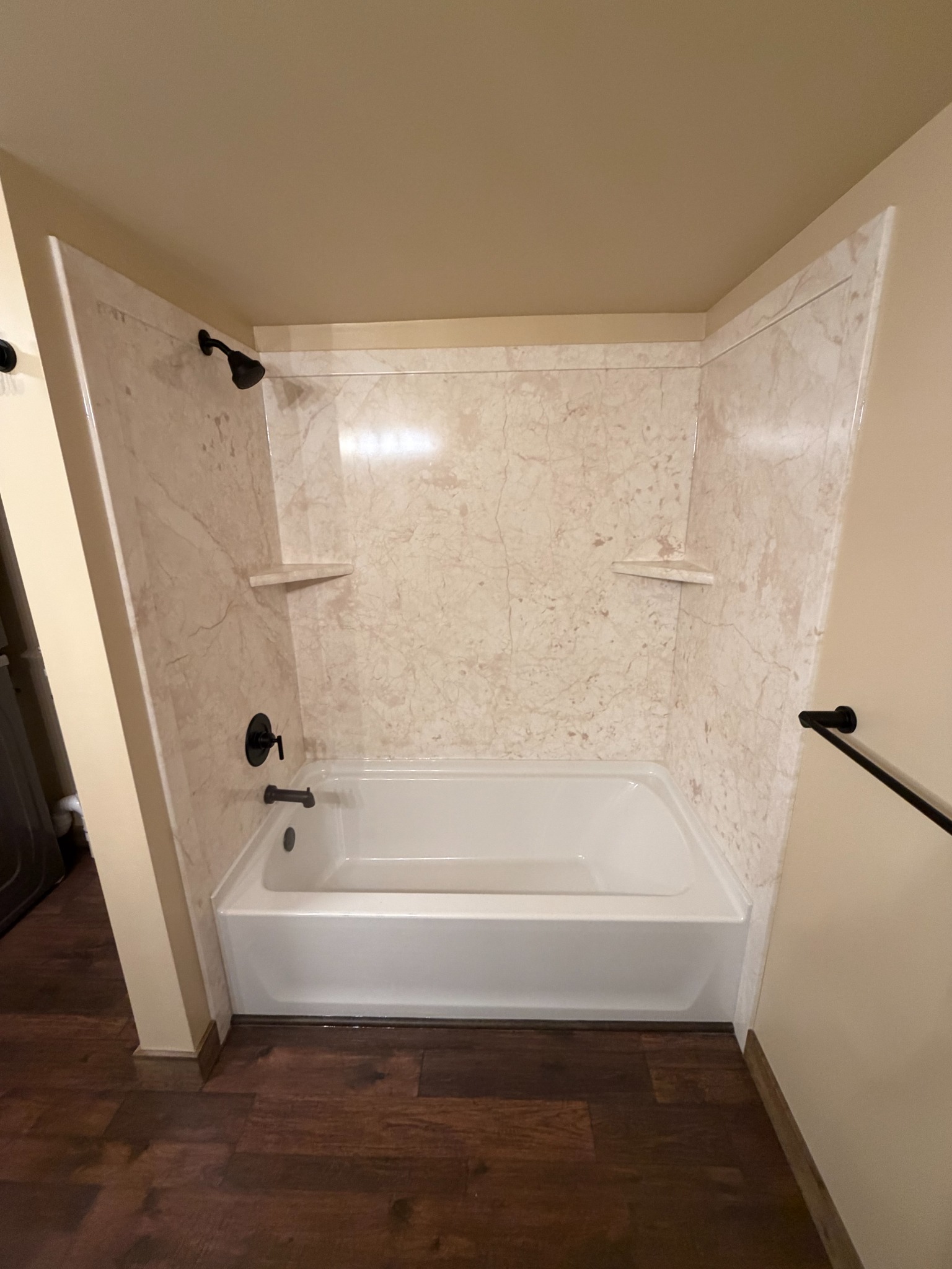 Completed bathtub with light stone-look wall surround and dark fixtures